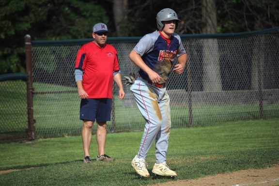 A baseball player prepares to field while a coach watches from behind.