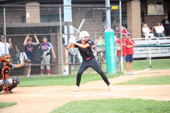A player at bat during a youth baseball game with spectators in the background.
